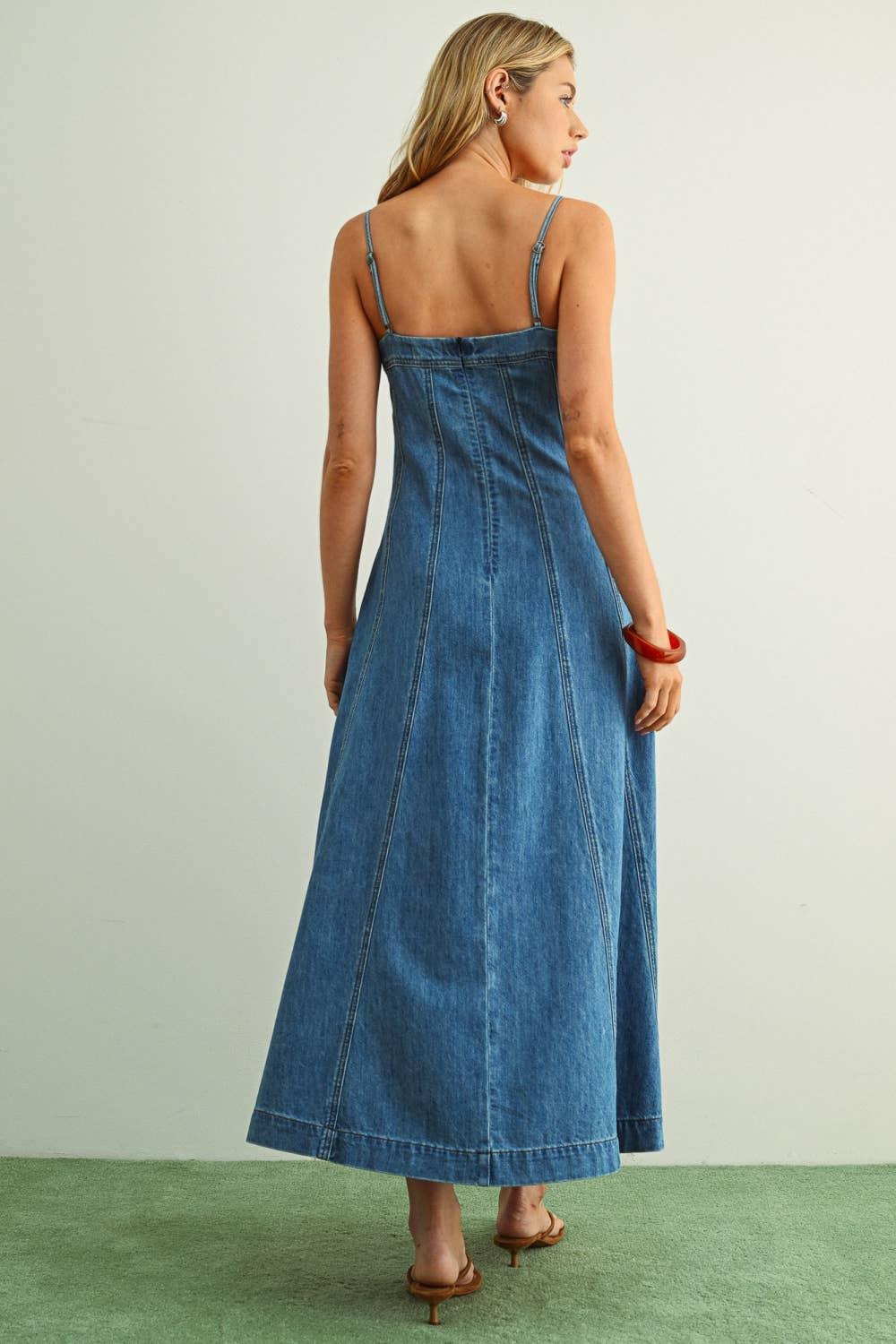 Woman wearing blue denim maxi dress with thin straps, back view, standing on green floor