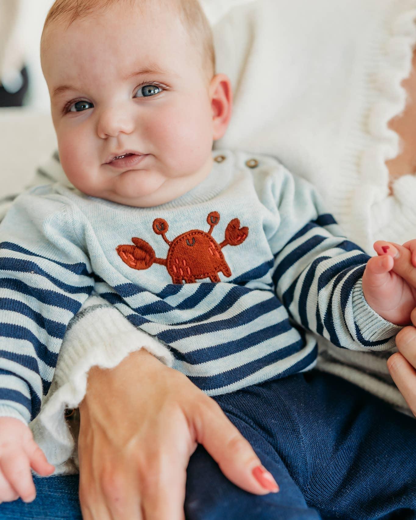 Baby in striped onesie with crab embroidery, cozy indoor setting
