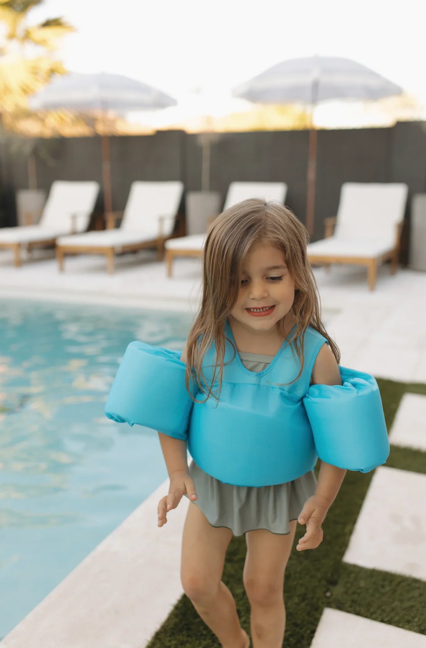 Child wearing blue floaties by poolside, enjoying swim time outdoors