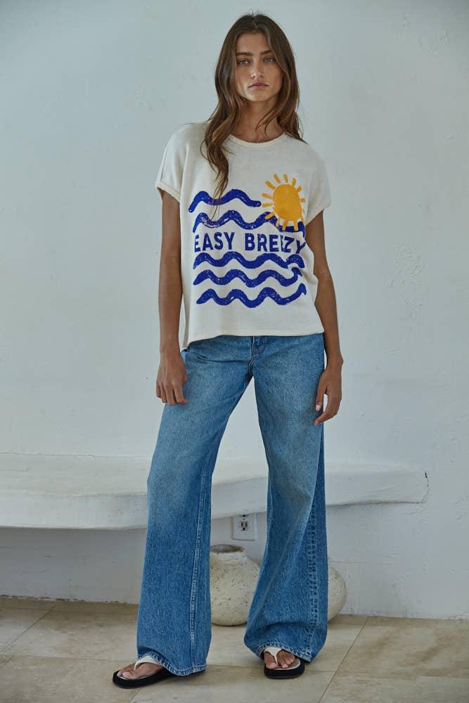 Woman wearing coastal graphic tee with 'Easy Breezy' waves and sun, paired with wide-leg jeans and flip flops