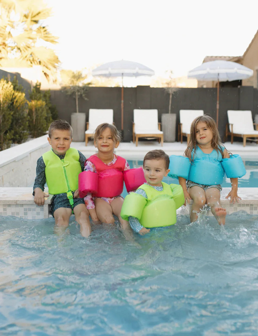 Kids in colorful swim vests playing by poolside with umbrellas and lounge chairs