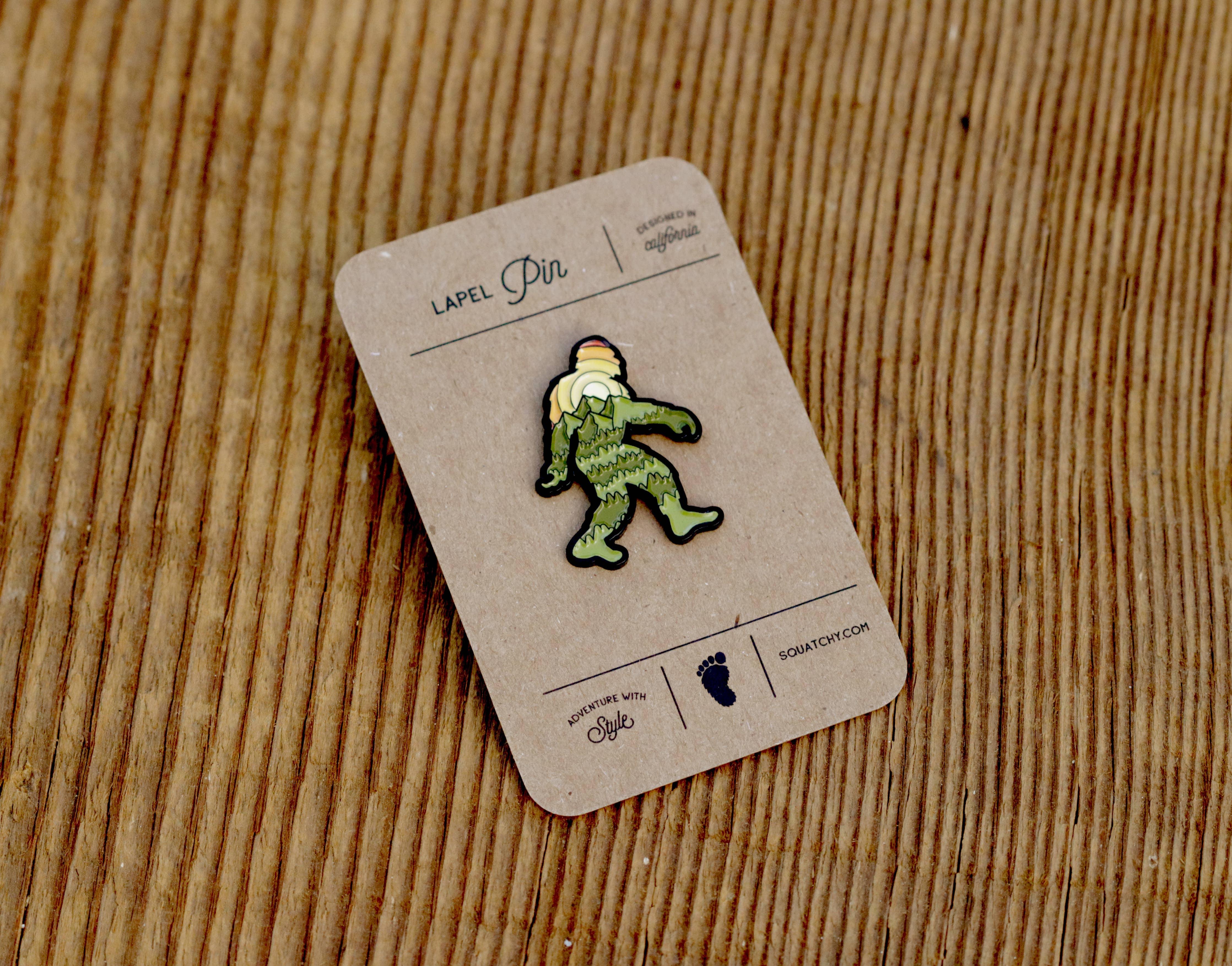 Green Sasquatch lapel pin on rustic wood, designed in California, adventure with style