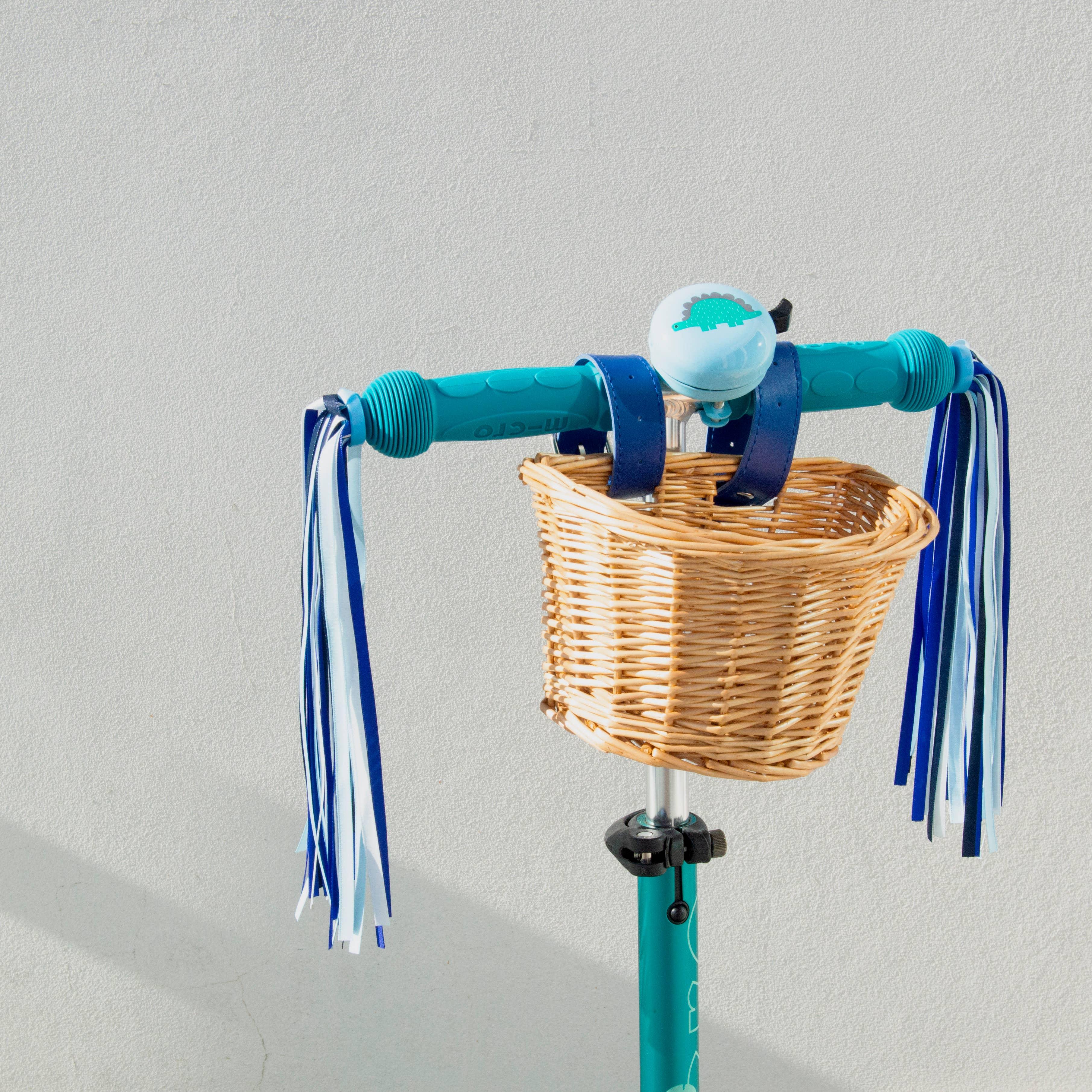 Teal bike handlebars with wicker basket, dinosaur bell, and blue-white streamers for coastal adventures.