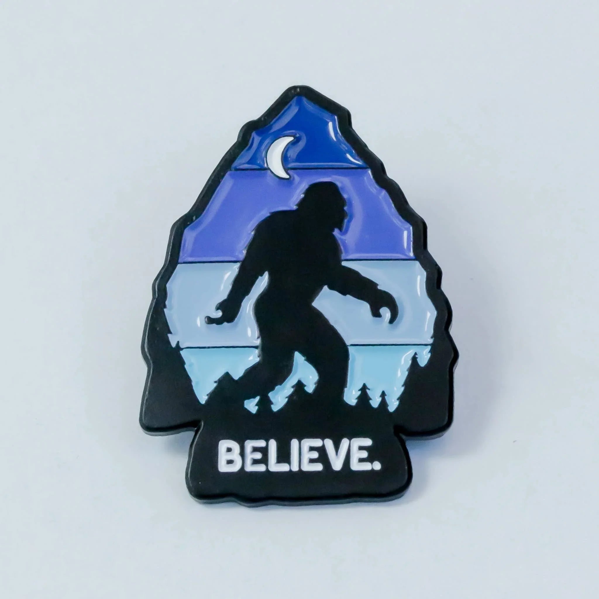 Bigfoot silhouette pin with 'BELIEVE' text, mountain, moon, and trees design