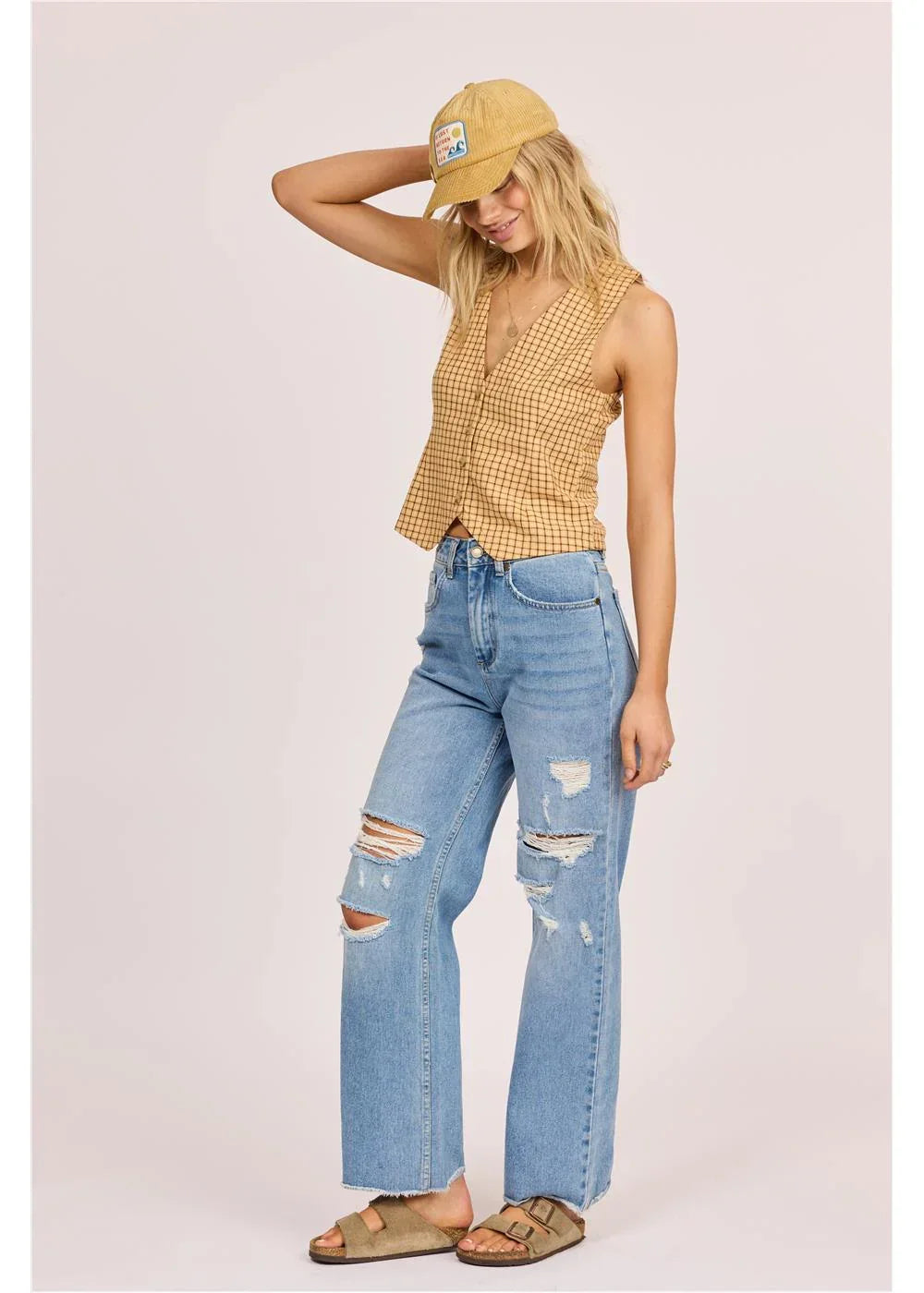 Woman in yellow plaid top, ripped jeans, and corduroy cap for coastal PNW style