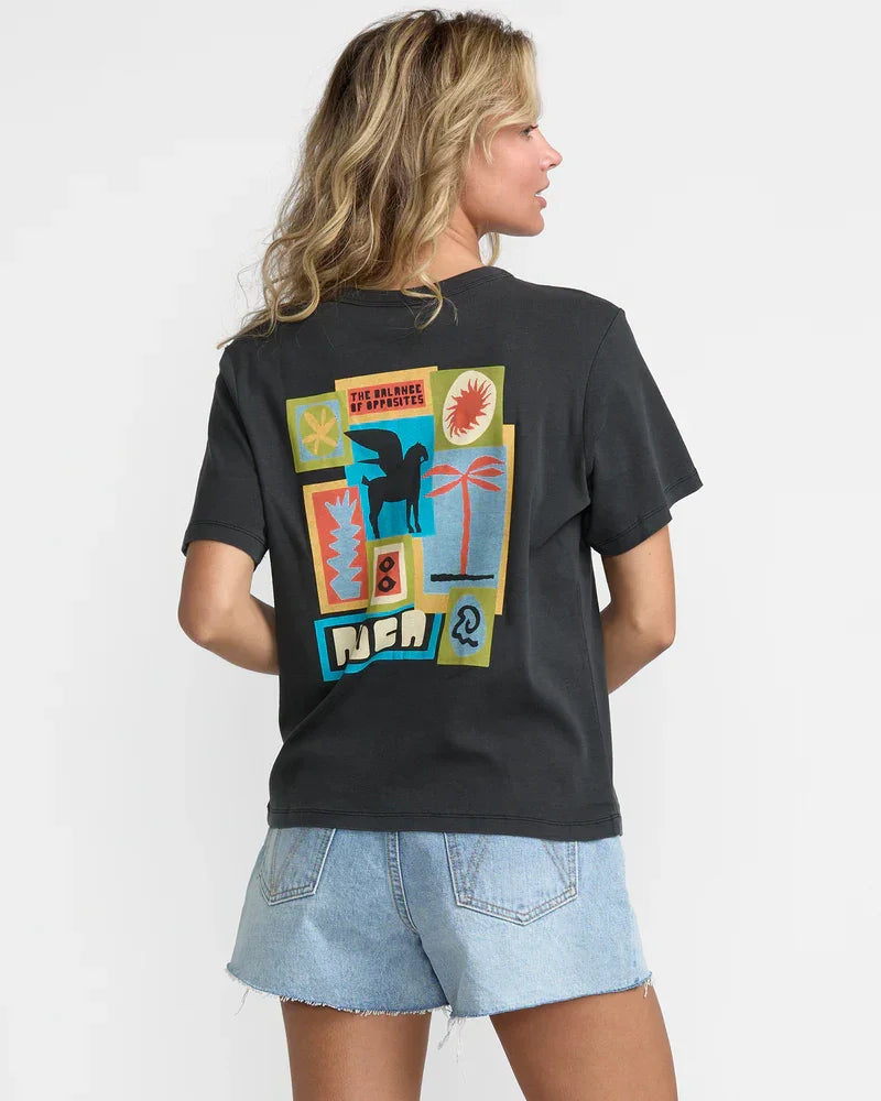 Woman wearing black graphic tee with colorful collage print, palm tree, and 'PURA VIDA' text, paired with denim shorts.