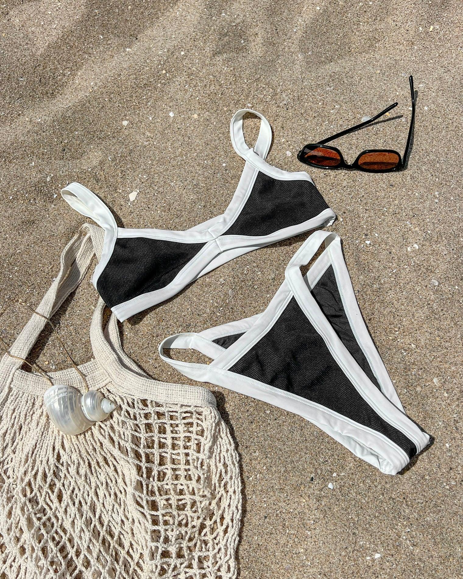 Black and white bikini set on sandy beach with sunglasses and mesh bag