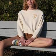 Woman in cream sweater and shorts sitting on bench, coastal outdoor style