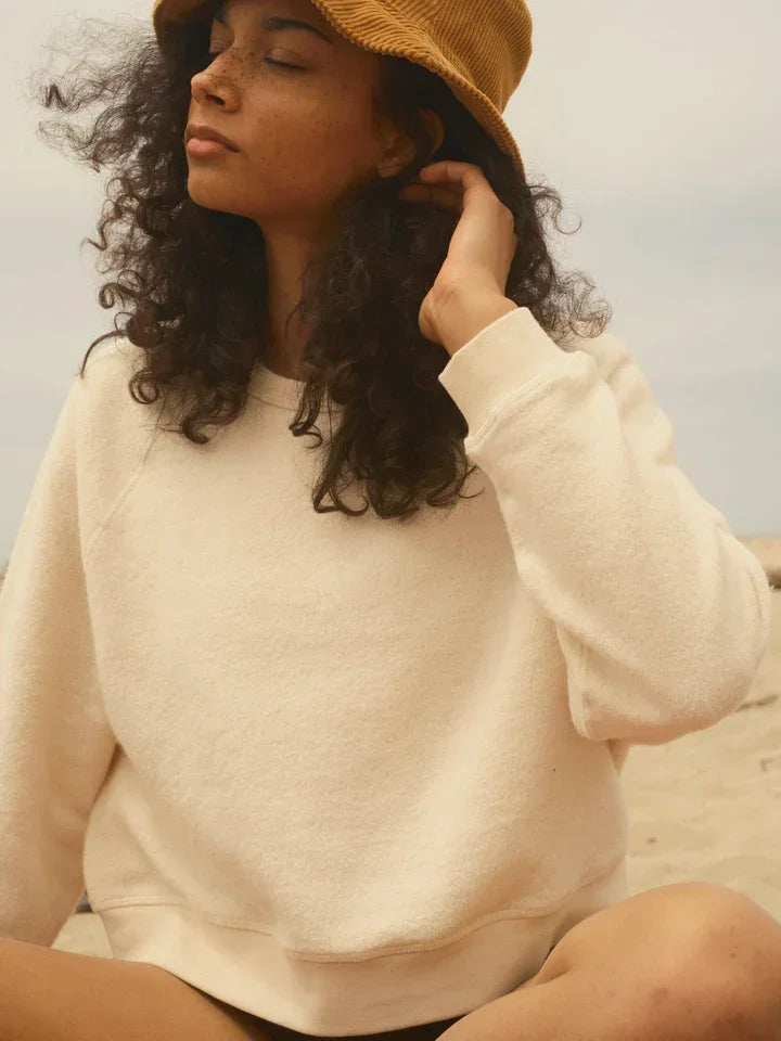 Woman in cozy cream sweatshirt and corduroy hat at beach, coastal PNW style