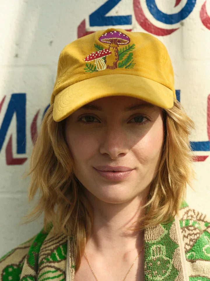 Yellow cap with embroidered mushrooms and green leaves, worn by woman outdoors