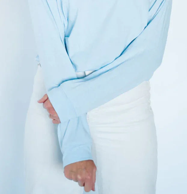 Light blue long-sleeve shirt with rolled cuffs, paired with white pants for coastal casual style