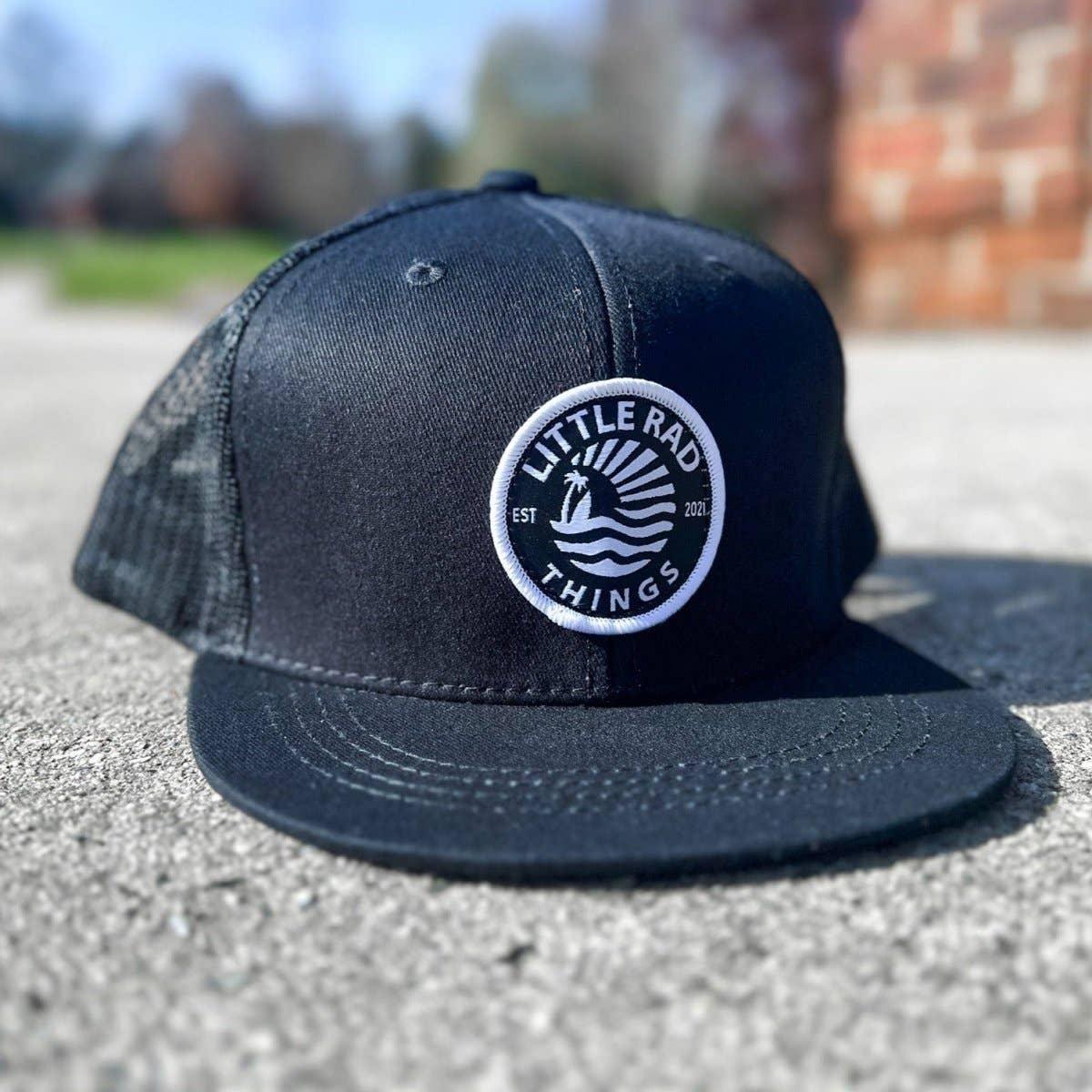 Black trucker hat with 'Little Rad Things' ocean logo, outdoor concrete setting