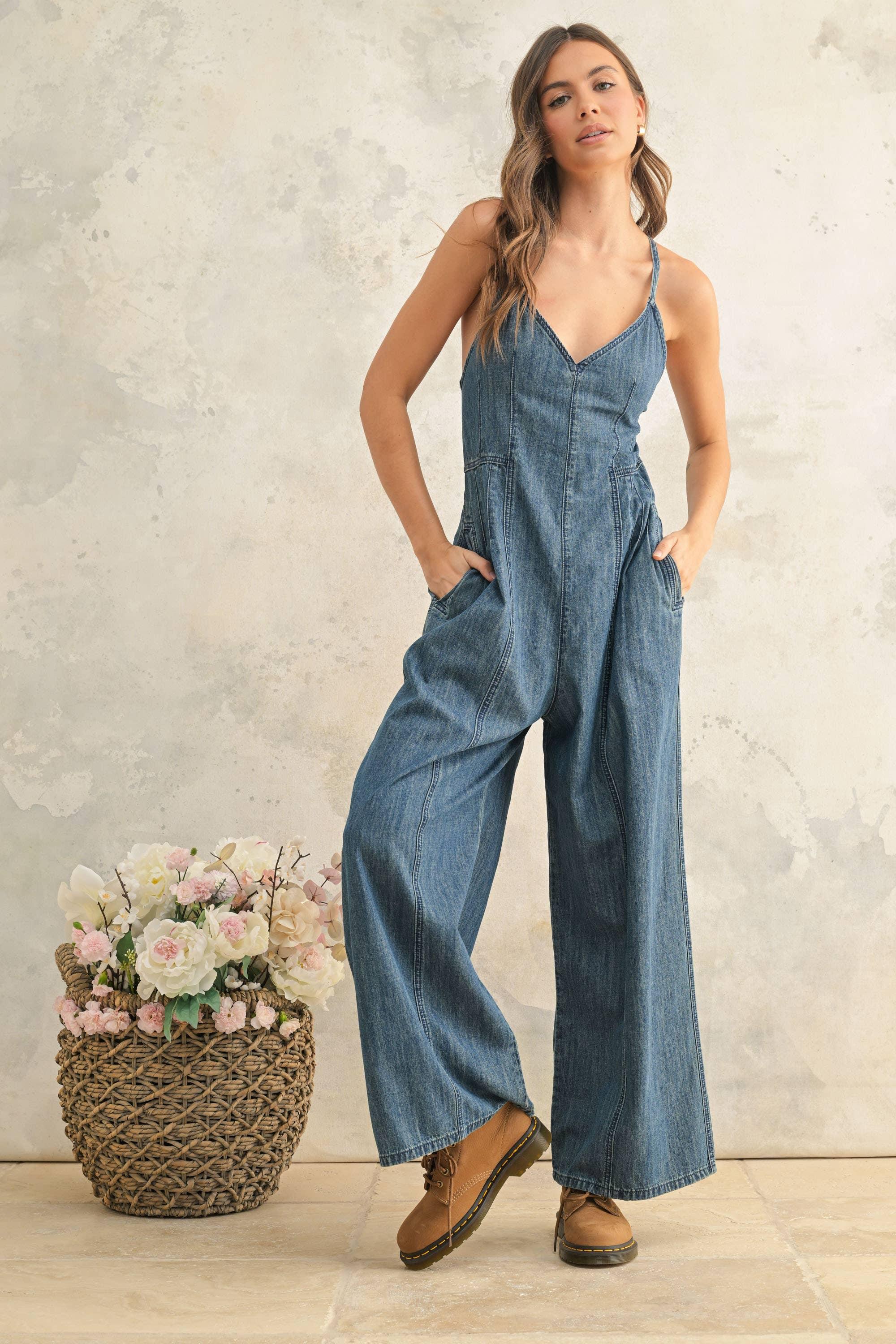Woman in denim jumpsuit with wide legs, hands in pockets, styled with brown boots and floral basket