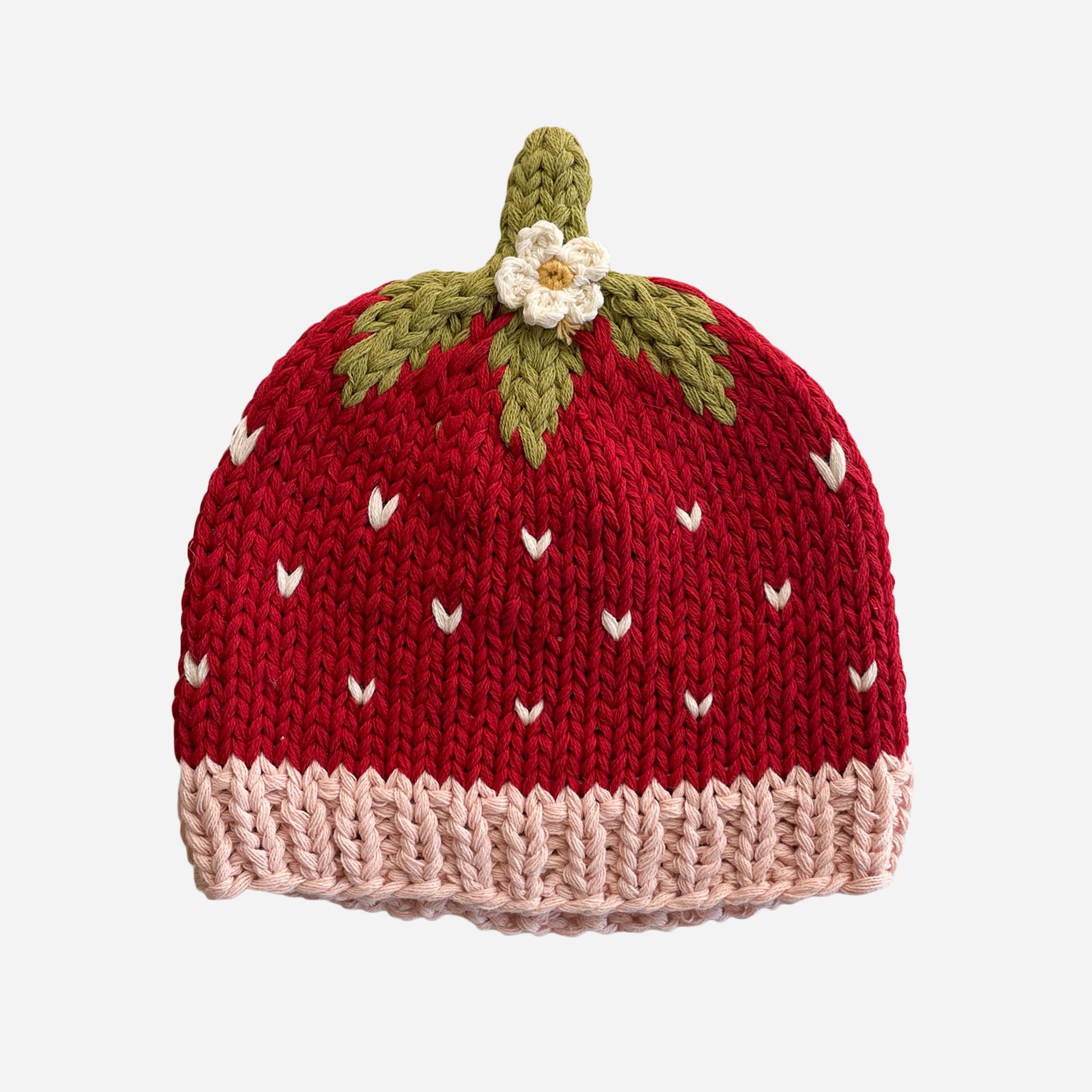 Knitted strawberry beanie with green leaves, white flower, and pink brim for cozy outdoor adventures.
