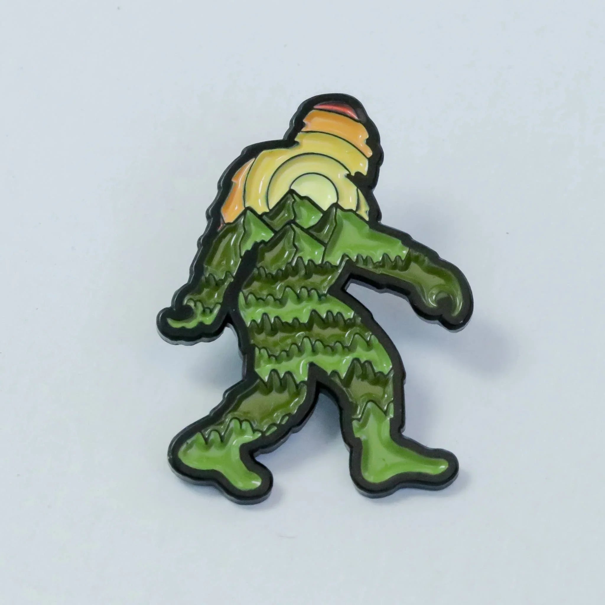 Green Bigfoot enamel pin with mountain and sunset design