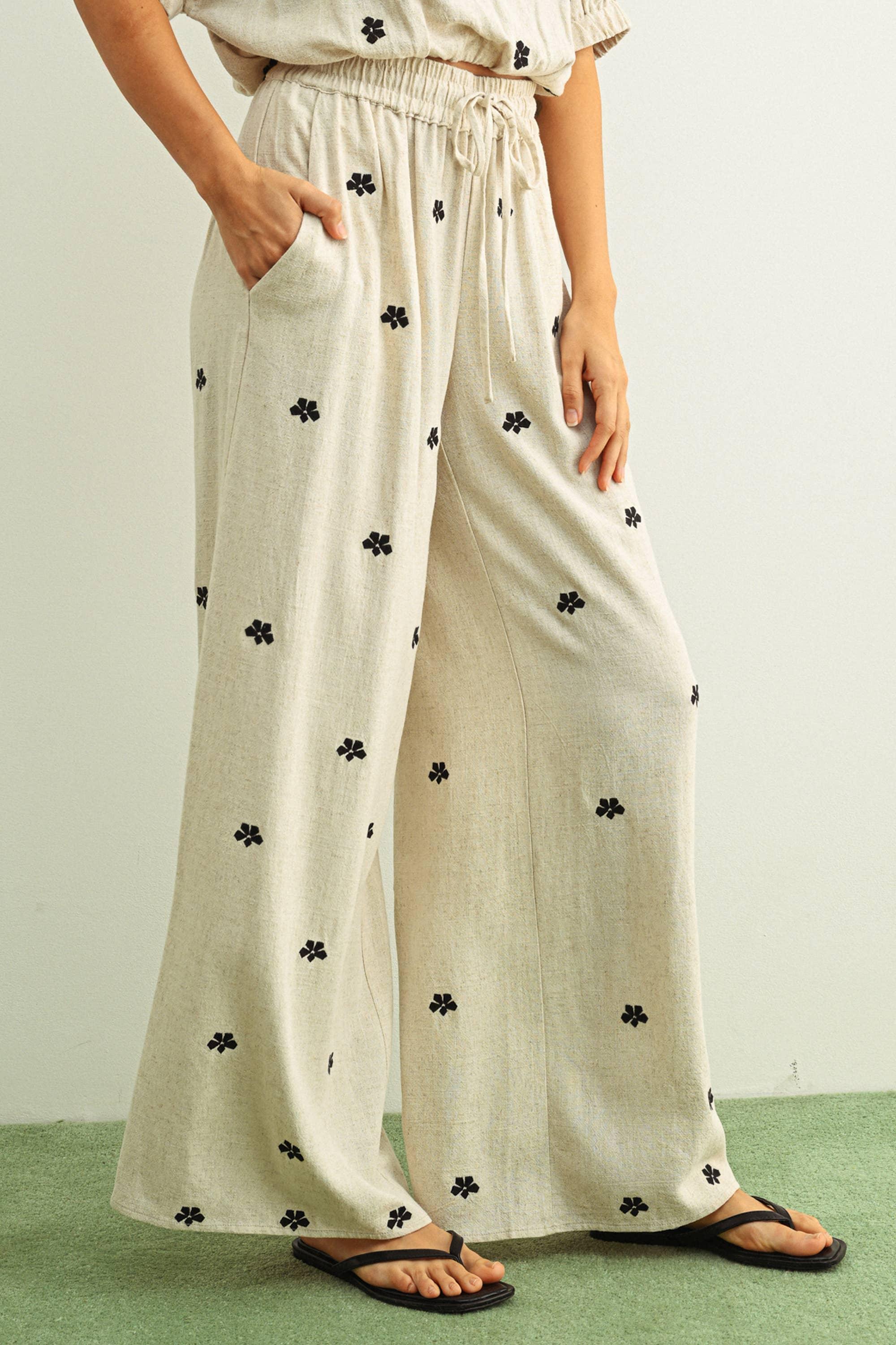 Cream wide-leg pants with black floral print, elastic waist, and side pockets, paired with flip flops
