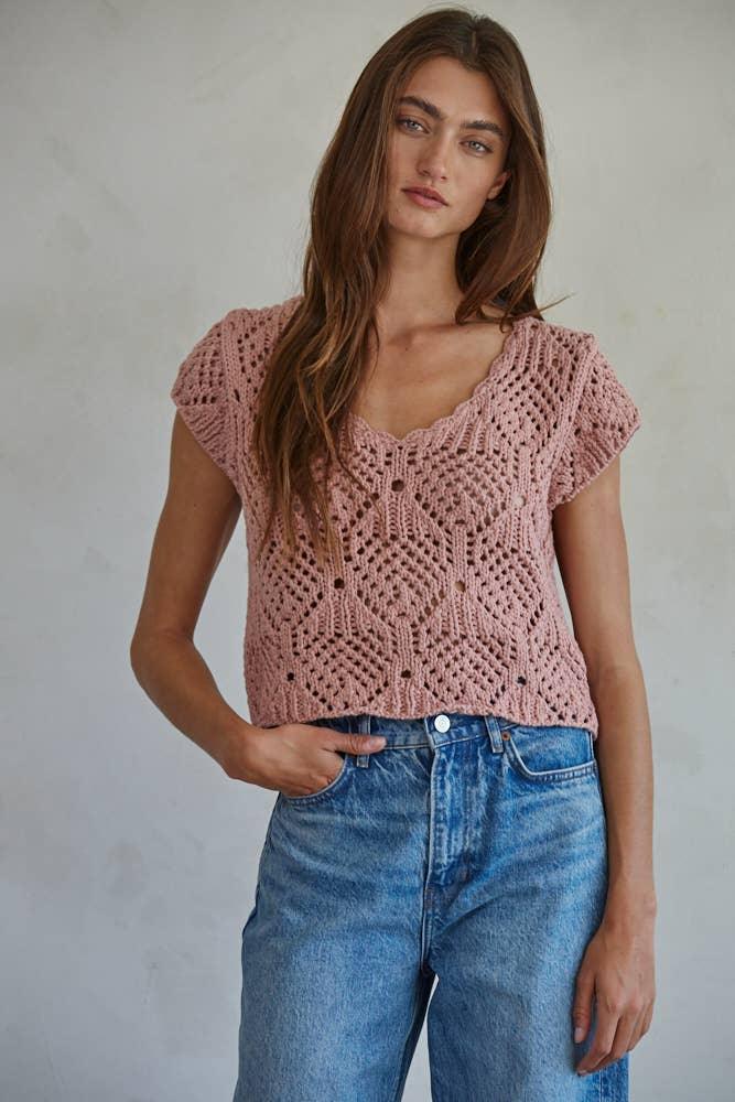 Woman wearing pink crochet knit top with V-neck and short sleeves, paired with blue jeans