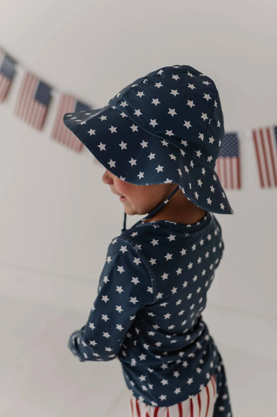 Child in navy star-print sun hat and matching rash guard, perfect for beach days and outdoor adventures.