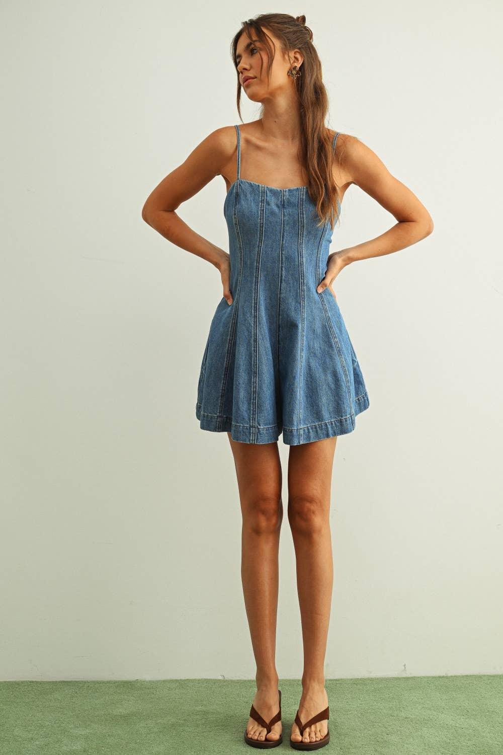 Woman in denim romper with thin straps and flared shorts, standing confidently on green carpet