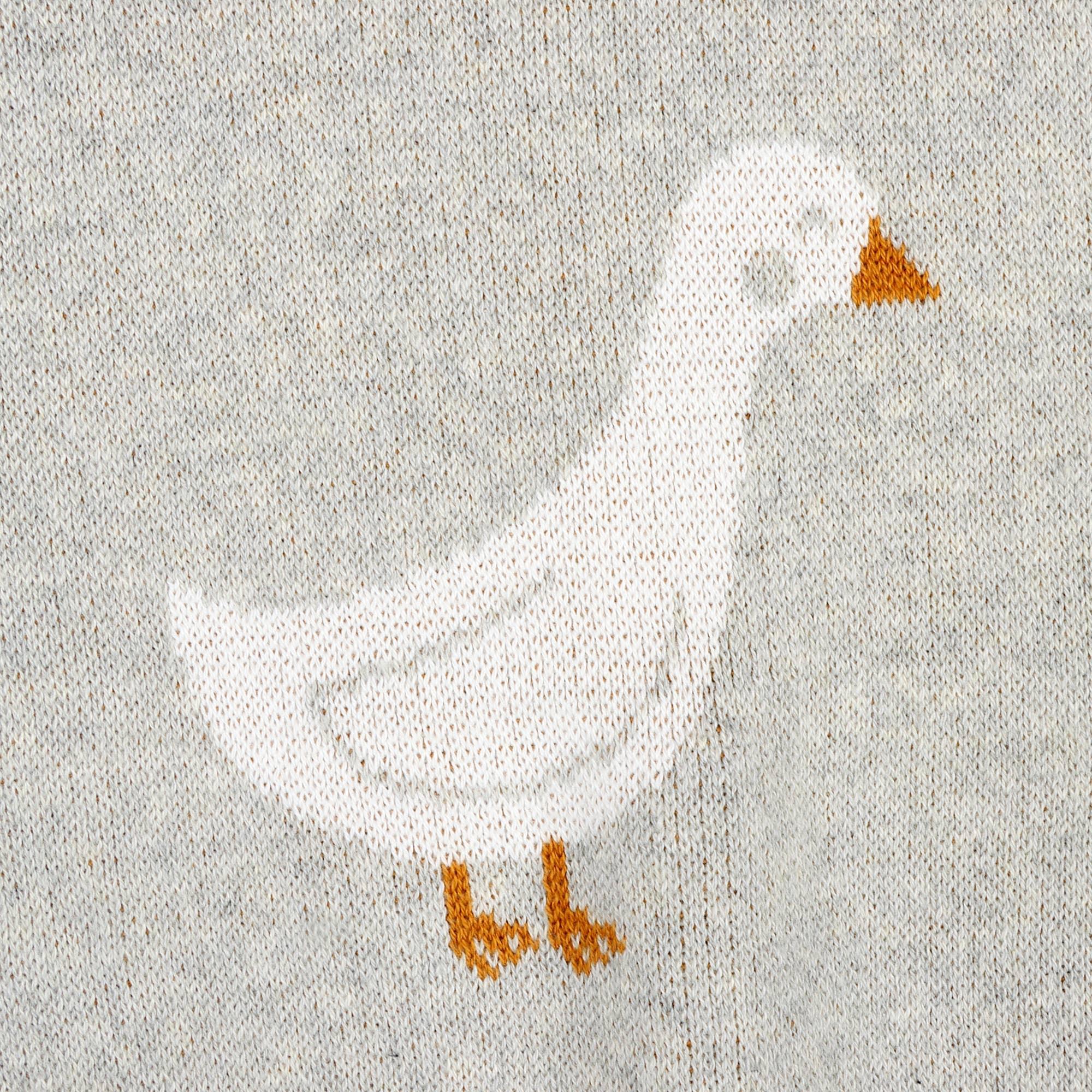 Knitted white goose with orange beak and feet on gray fabric, cozy outdoor apparel detail