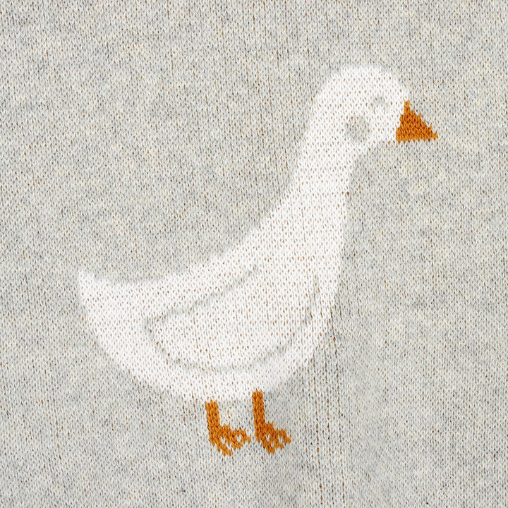 Knitted white goose with orange beak and feet on gray fabric, cozy outdoor apparel detail