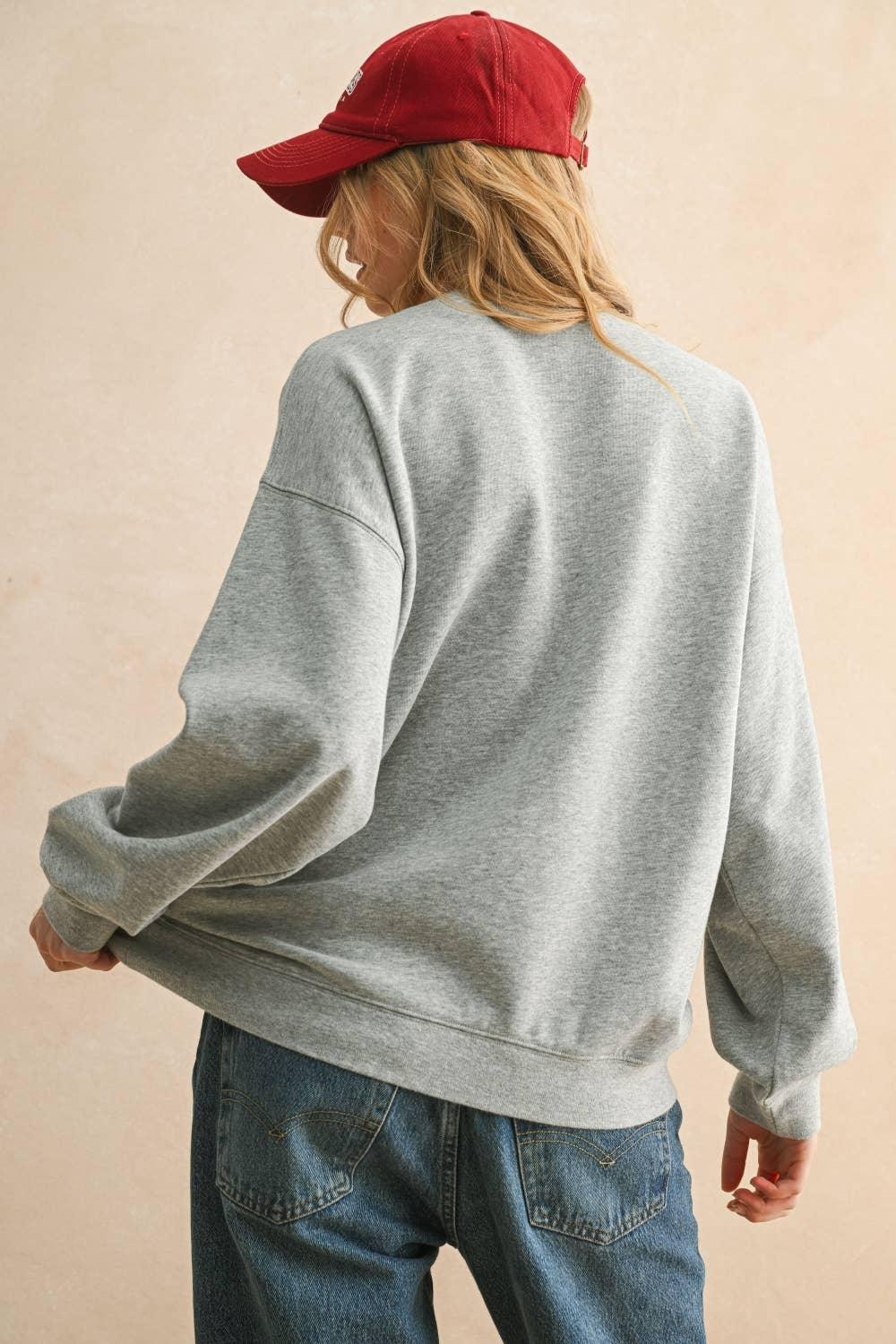 Rear view of a person wearing a grey MIOU MUSE oversized sweatshirt and red baseball cap.