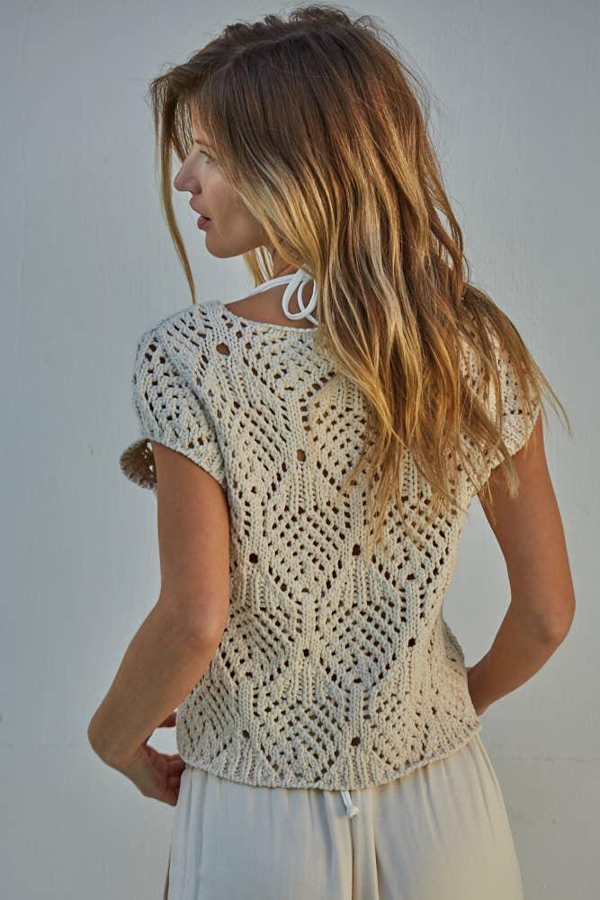 Woman wearing cream crochet top with open back design and short sleeves, paired with light skirt