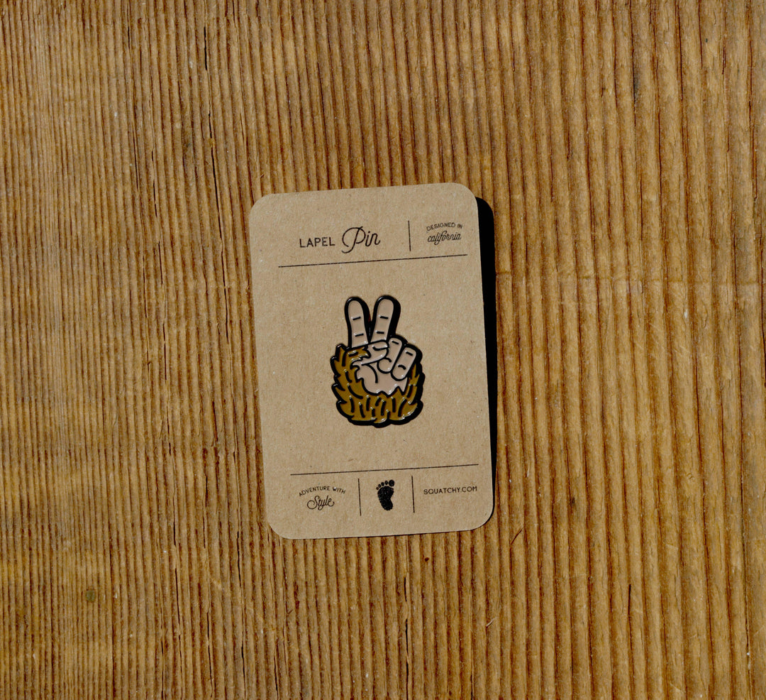 Squatchy Bigfoot Peace enamel lapel pin on a brown cardboard backing.