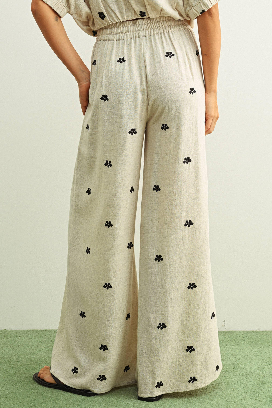 Beige wide-leg pants with black floral print, elastic waist, paired with matching top and sandals