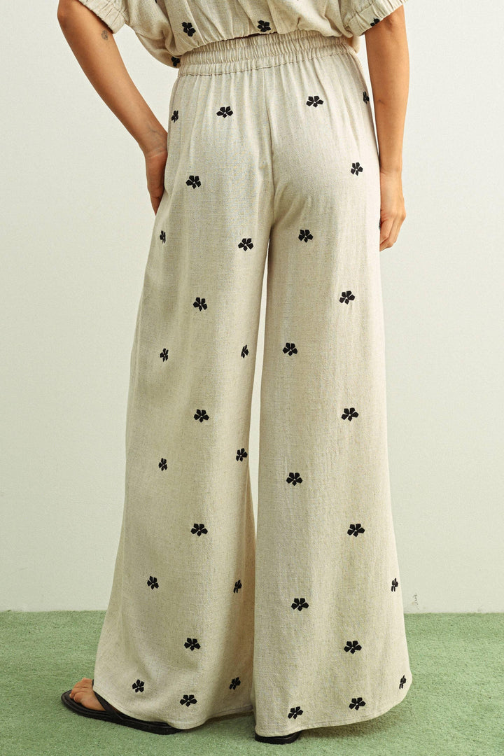 Beige wide-leg pants with black floral print, elastic waist, paired with matching top and sandals