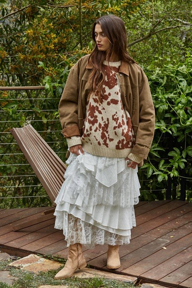 Woman in cow print sweater, tiered lace skirt, and tan boots on wooden deck, coastal PNW style