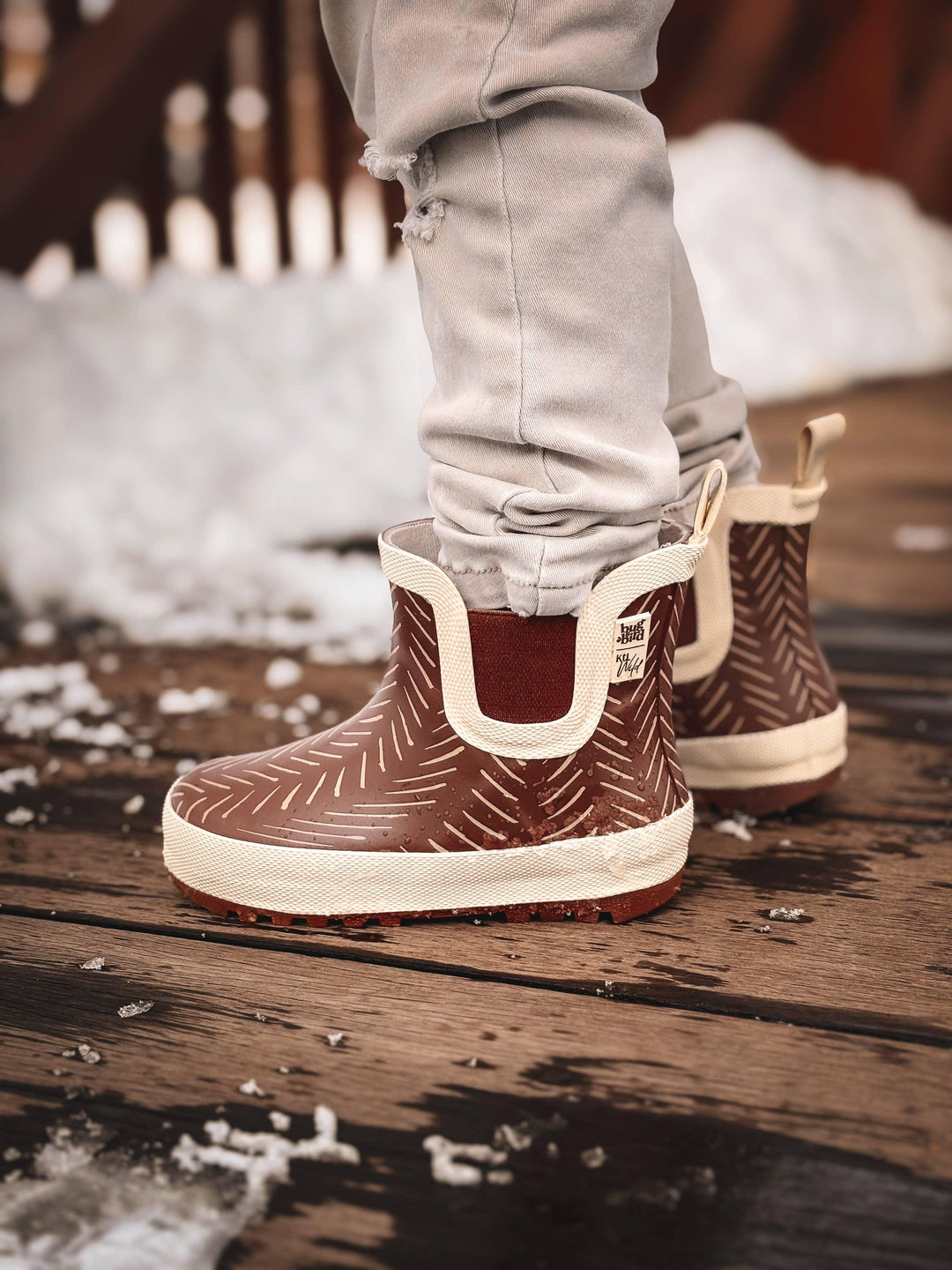 Brown herringbone rain boots with cream trim, worn on snowy wooden deck, perfect for PNW adventures.