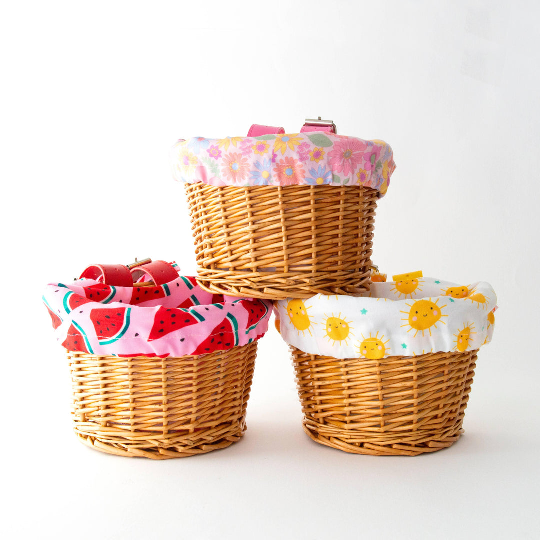 Three wicker bike baskets with colorful liners: watermelon, sun, and floral patterns for outdoor adventures.