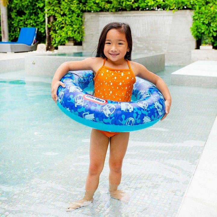Child holding blue swim ring with car patterns by poolside
