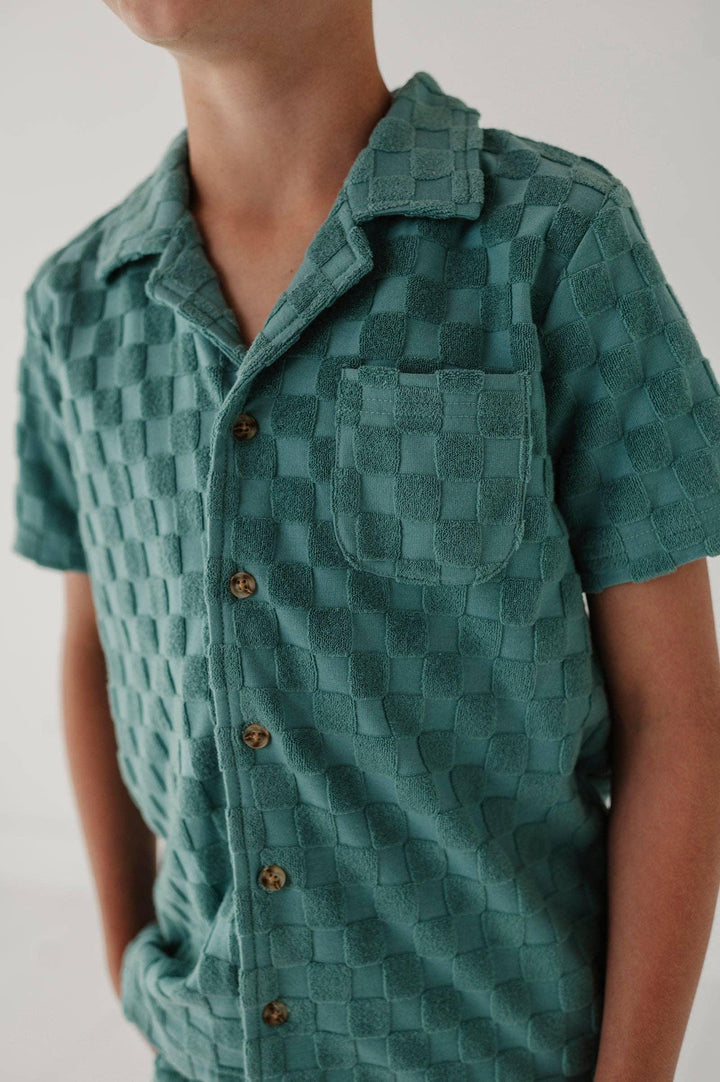 Teal short-sleeve checkered button-up shirt with chest pocket, coastal style for beach days and outdoor adventures.