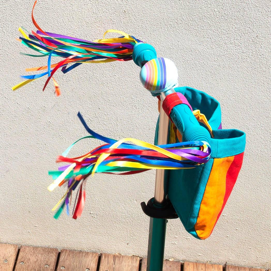 Colorful rainbow streamers on a scooter handlebar with matching bag, perfect for outdoor fun and coastal adventures.