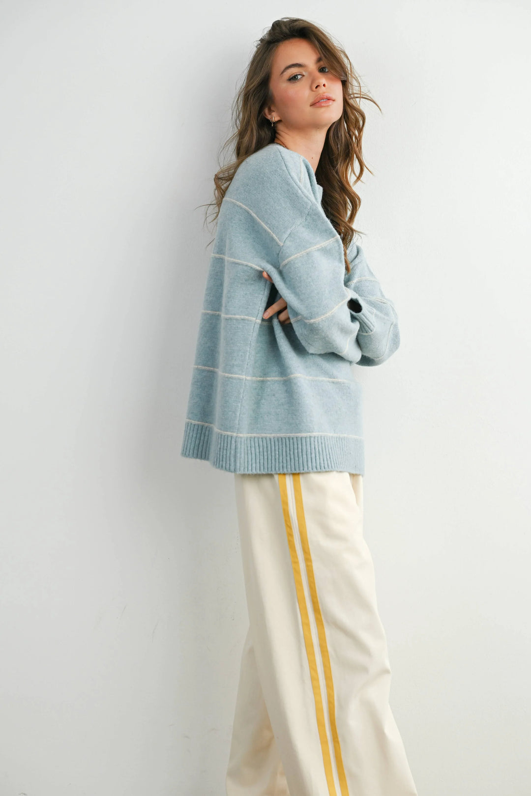 Woman in light blue striped sweater and cream pants with yellow side stripes, coastal style outfit