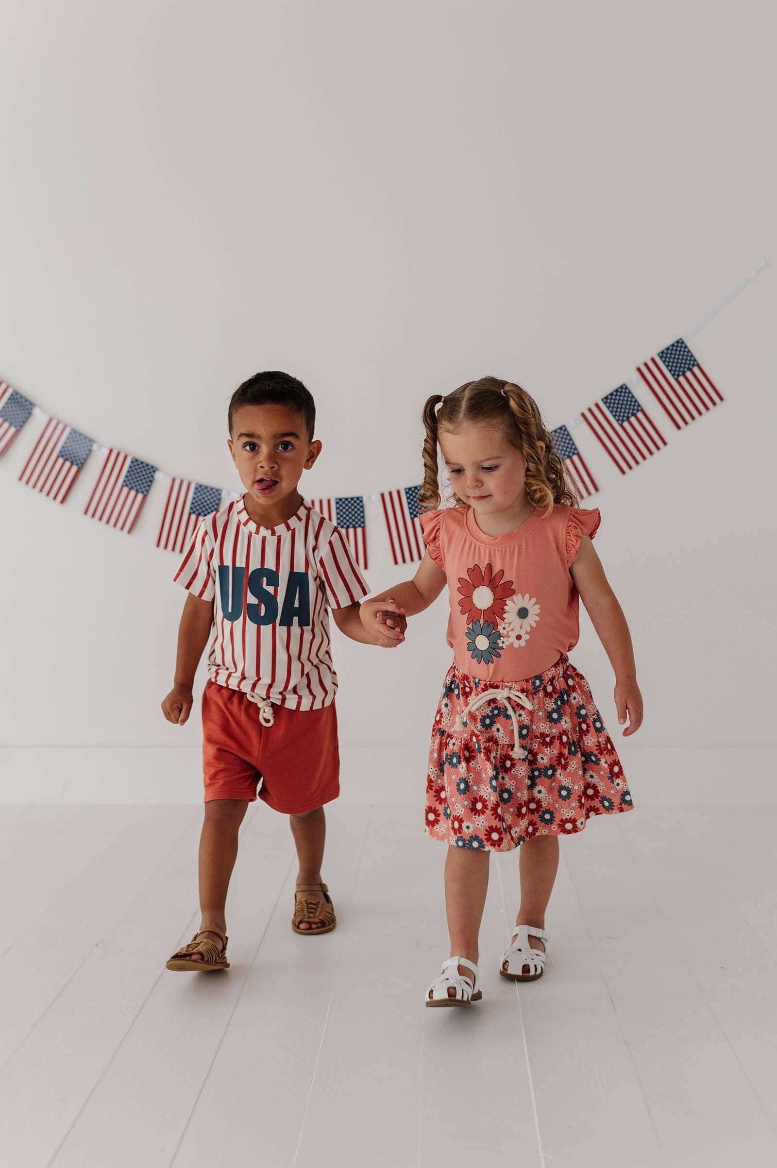 Kids in USA-themed summer outfits with flag banner, perfect for coastal adventures and beach days