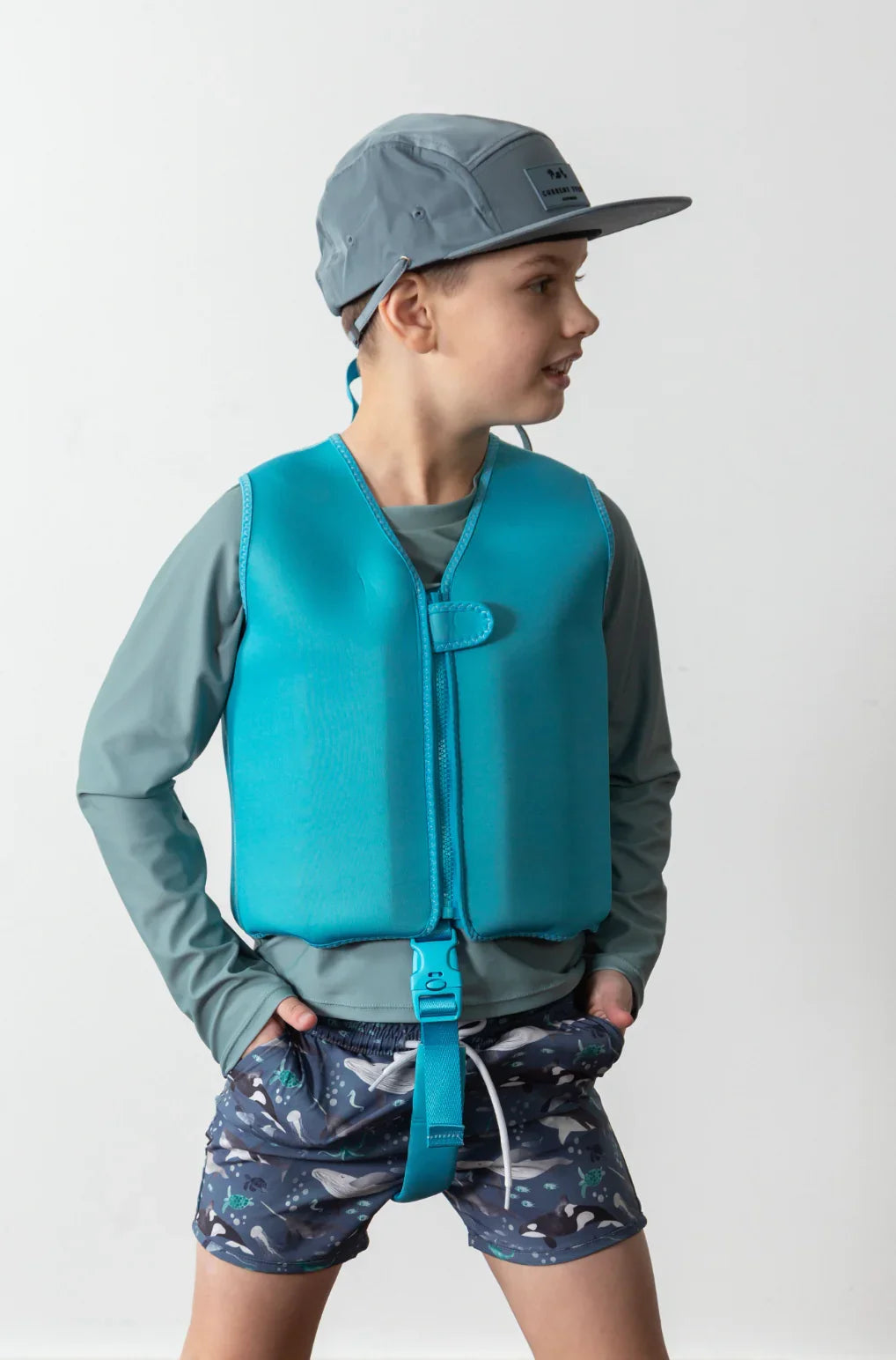 Child wearing teal life vest, gray cap, and whale-print swim shorts for water safety