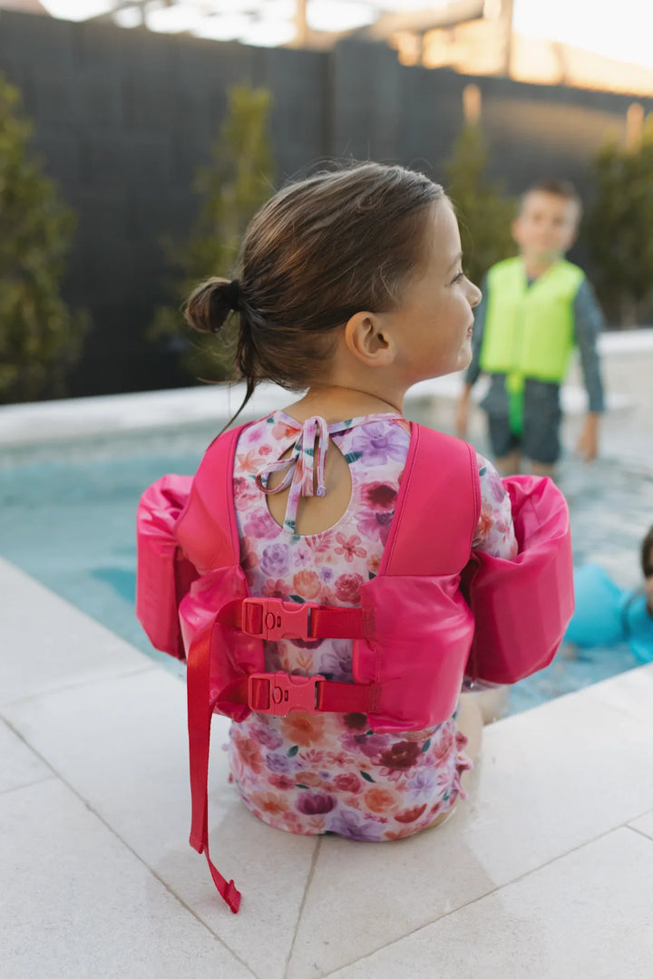 Toddler girl in pink float vest by pool, floral swimsuit, safe swim gear for kids