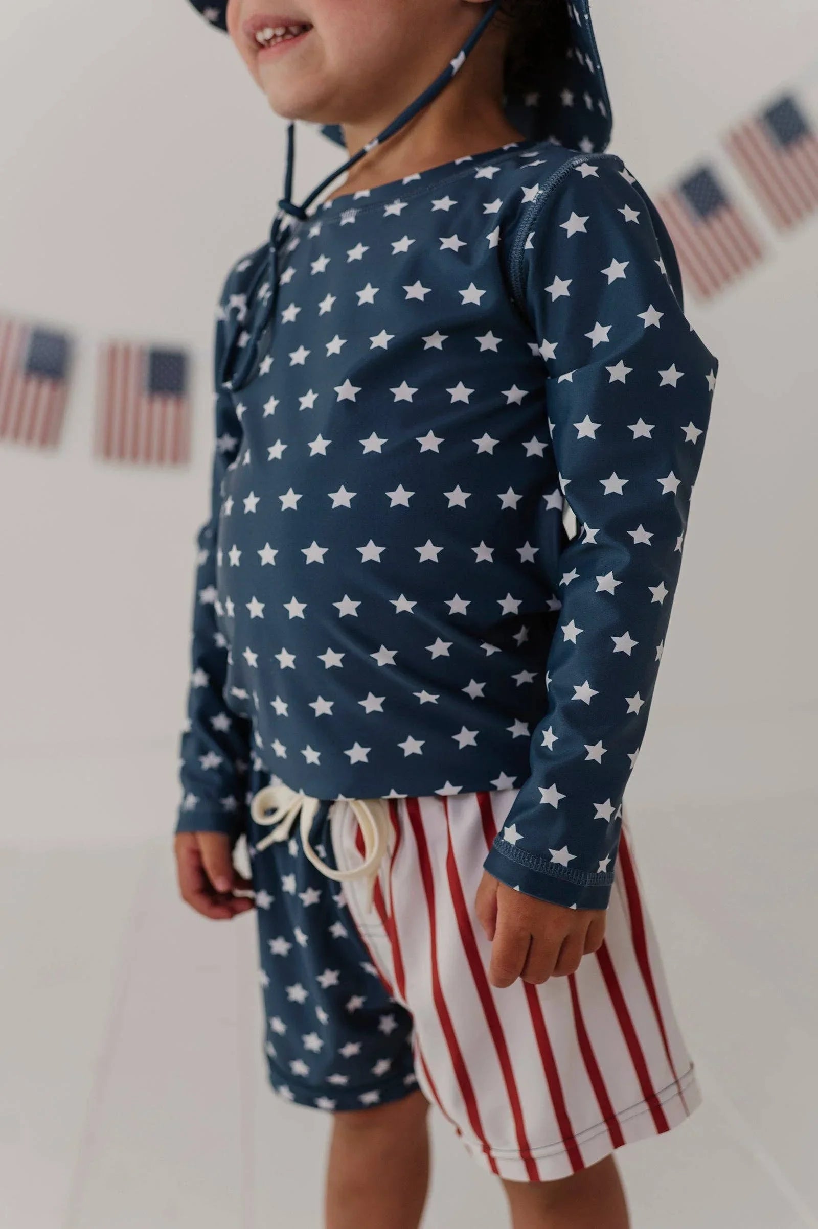 Child in navy star rash guard and red-white striped swim trunks, perfect for beach days and outdoor adventures.