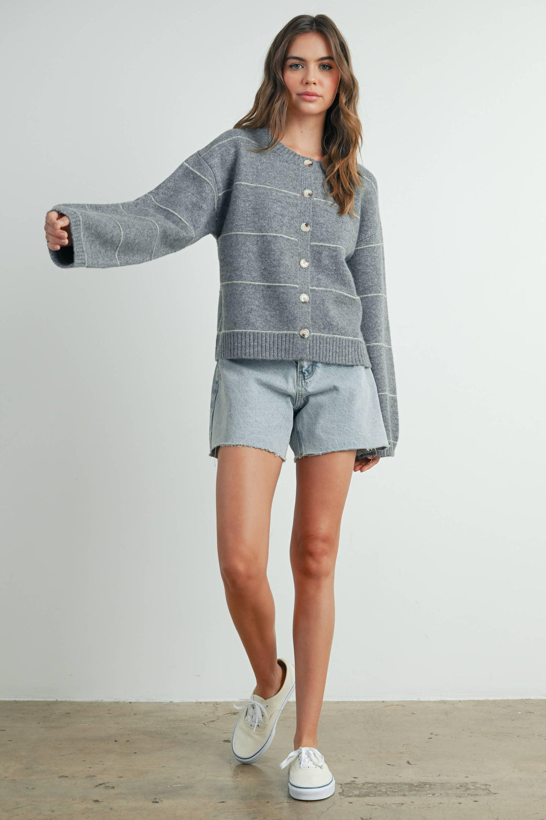 Woman in gray striped button-up cardigan, denim shorts, and white sneakers for casual coastal style