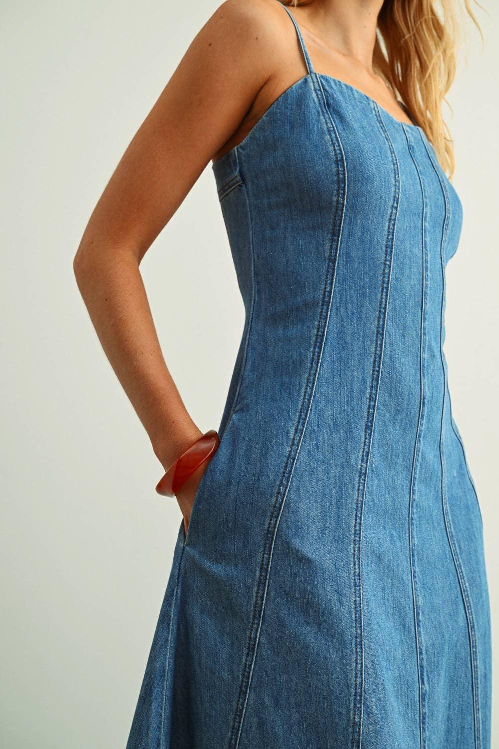 Blue denim sundress with thin straps and side pockets, worn by woman with hand in pocket