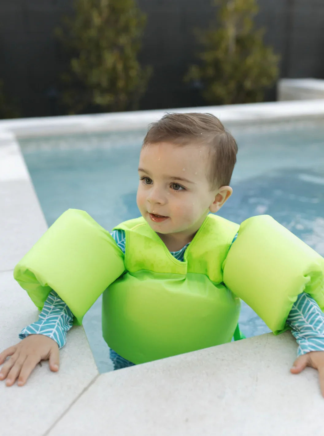 Toddler in green float vest at pool edge, learning to swim safely