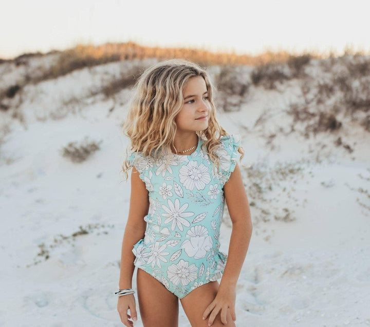 Girl in floral one-piece swimsuit on sandy beach, coastal summer style