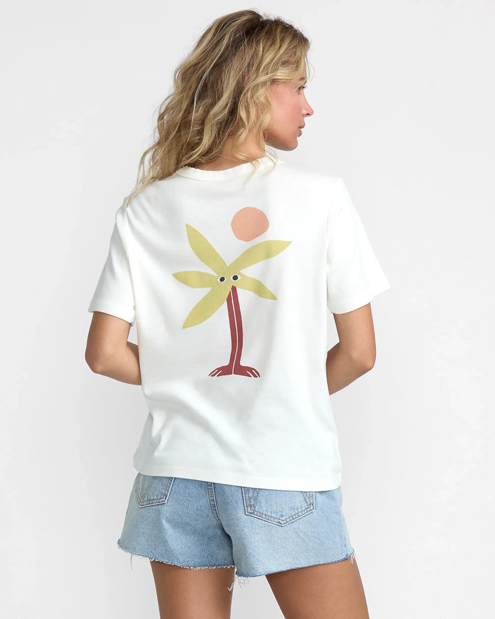 Back view of a woman wearing a white RVCA Daily Tee with a stylized palm tree graphic.