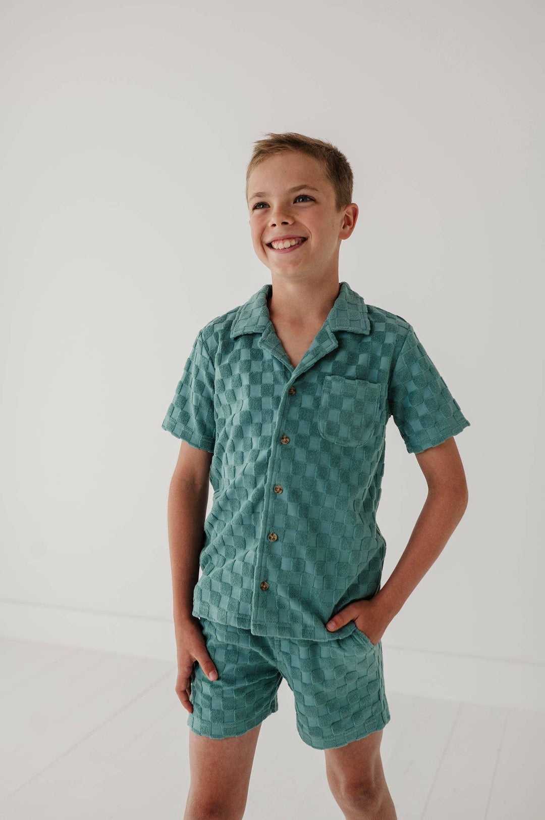 Boy in teal checkered short sleeve pajama set with button front and pocket, cozy sleepwear for kids