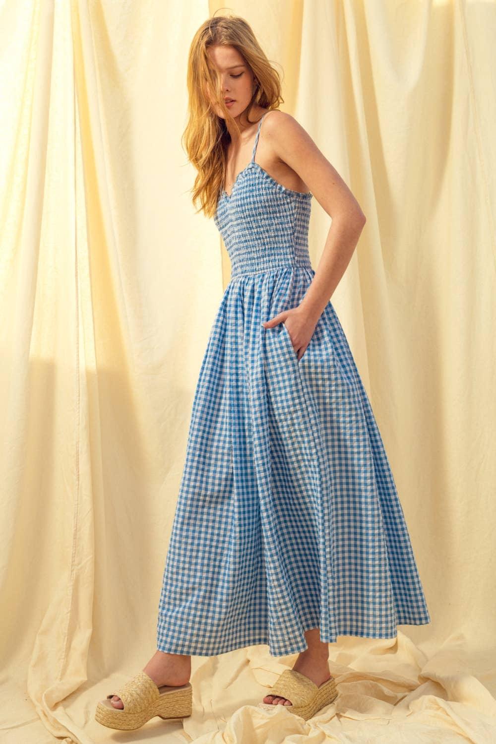 Woman in blue gingham midi dress with smocked bodice and espadrille wedges, standing against cream backdrop