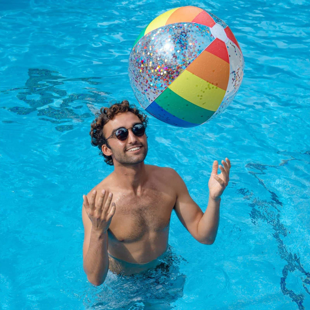 Man in pool with rainbow glitter beach ball, enjoying summer fun and outdoor lifestyle