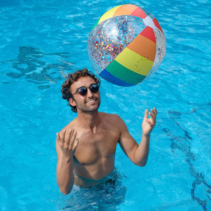 Man in pool with rainbow glitter beach ball, enjoying summer fun and outdoor lifestyle
